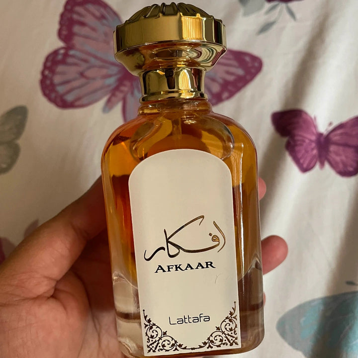 Perfume bottle labeled 'Afkaar' by Lattafa held in a hand with a butterfly-patterned background.