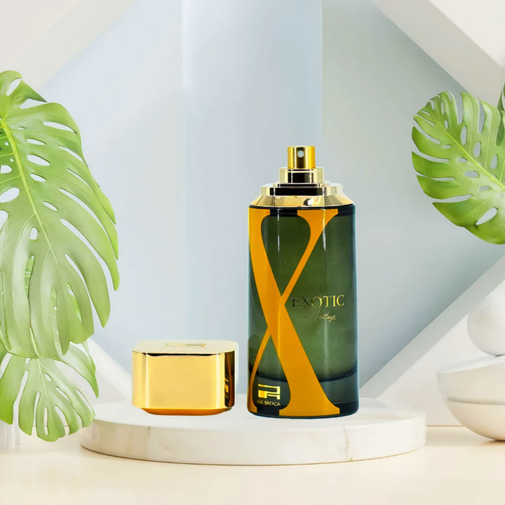 Afnan Rue Broca Exotic Heritage perfume bottle with gold cap on a white surface with green leaves in the background