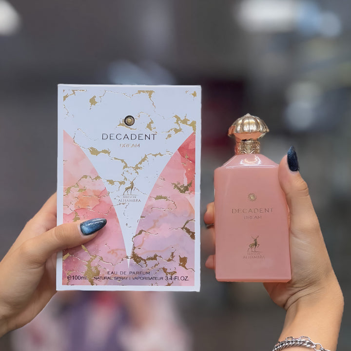 Pink 'Decadent' perfume bottle and packaging held by a person with a blurred background