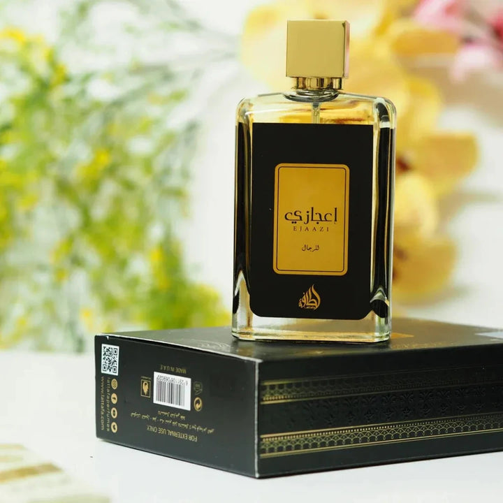 Perfume bottle with gold cap and black packaging on a white surface with blurred floral background