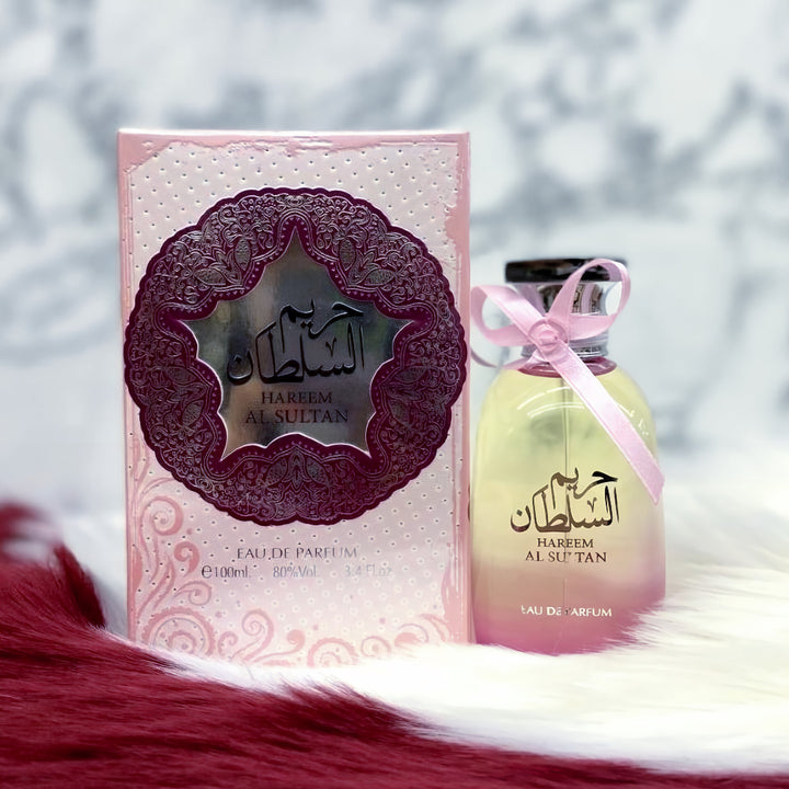 Harfem Al Sultan perfume bottle and packaging with a decorative pink ribbon against a blurred natural background.