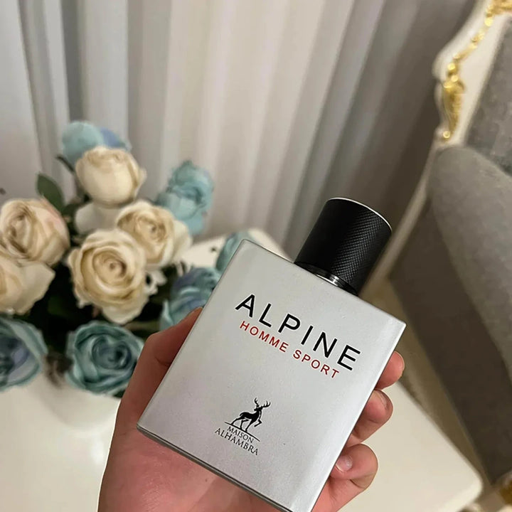 Hand holding a bottle of Alpine Homme Sport perfume with flowers in the background