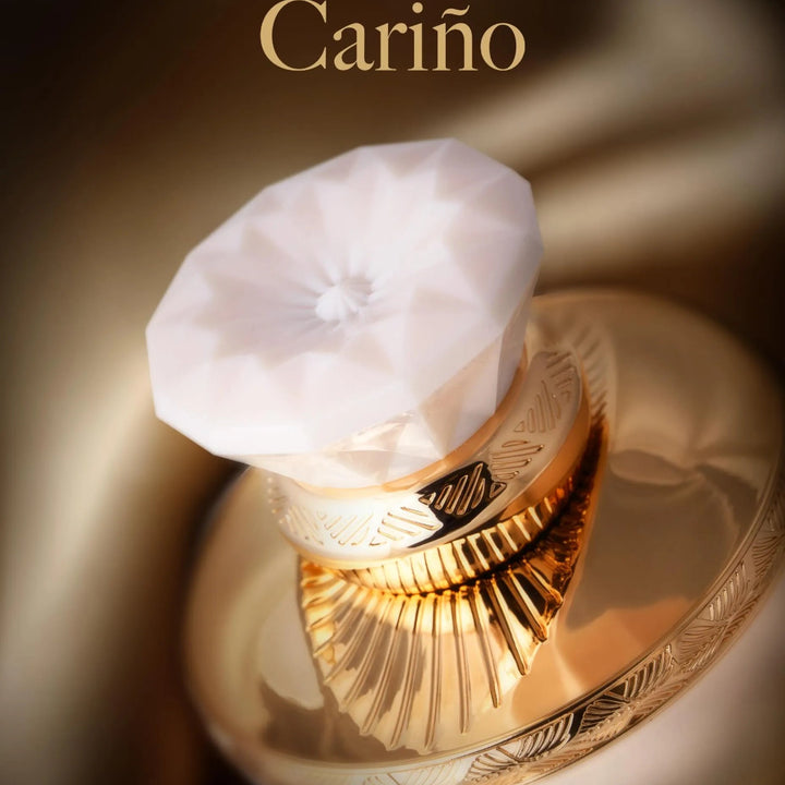 Perfume bottle with a white cap and gold accents on a dark background, featuring the brand 'Cariño'.