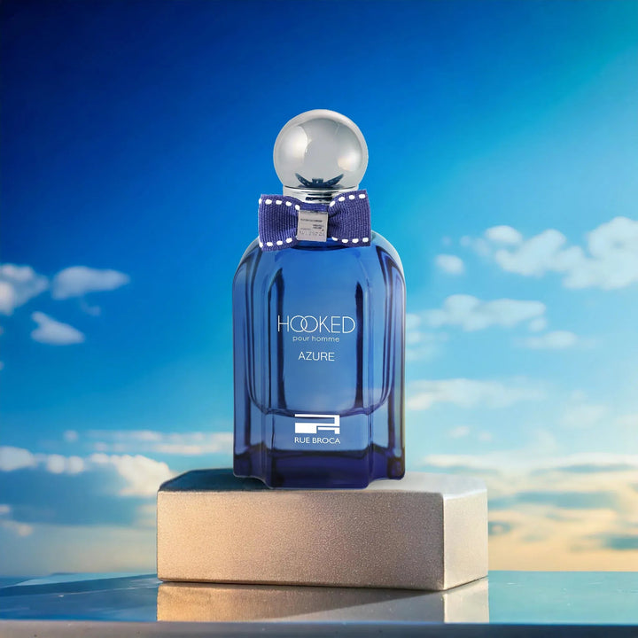 Blue perfume bottle labeled 'Hooked Azure' on a platform with a blue sky background