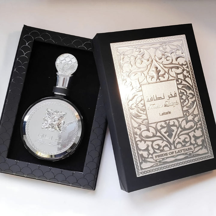 Lattafa fakhar silver perfume bottle with intricate design in a black box on a white background