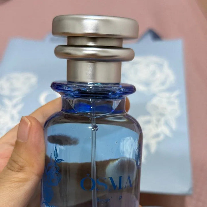 Blue glass bottle with silver cap held by a hand against a blurred background