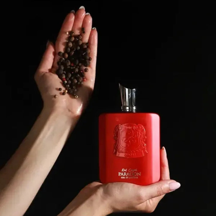Red perfume bottle held by a hand with pepper on a black background