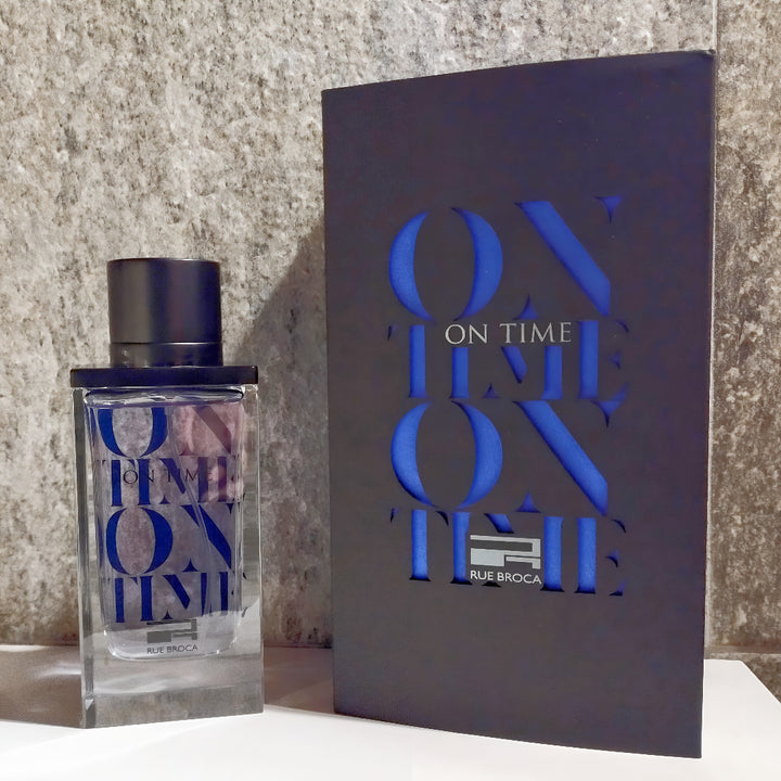 Perfume bottle and packaging with 'On Time pour Homme Rue Broca' branding on a textured surface