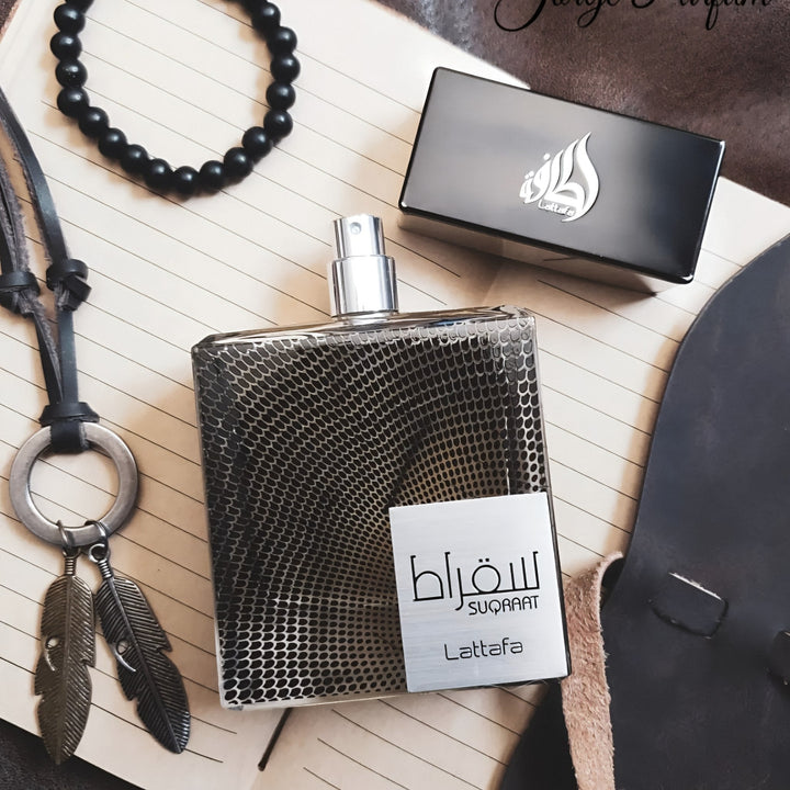 Perfume bottle with packaging and accessories on a textured surface suqraat lattara