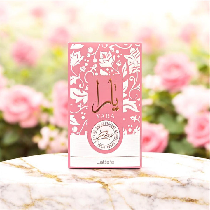 Pink Yara perfume box on a marble surface with blurred flowers in the background